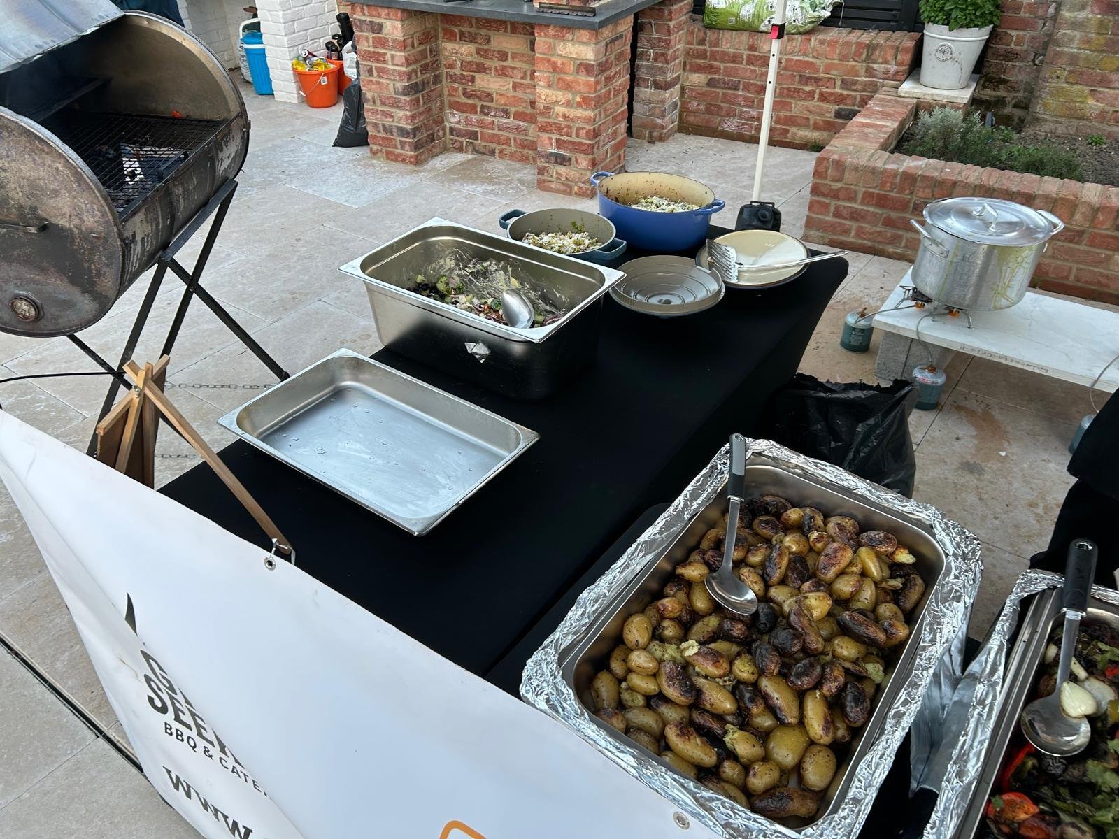 Outdoor food station with roasted potatoes, salads and a BBQ smoker
