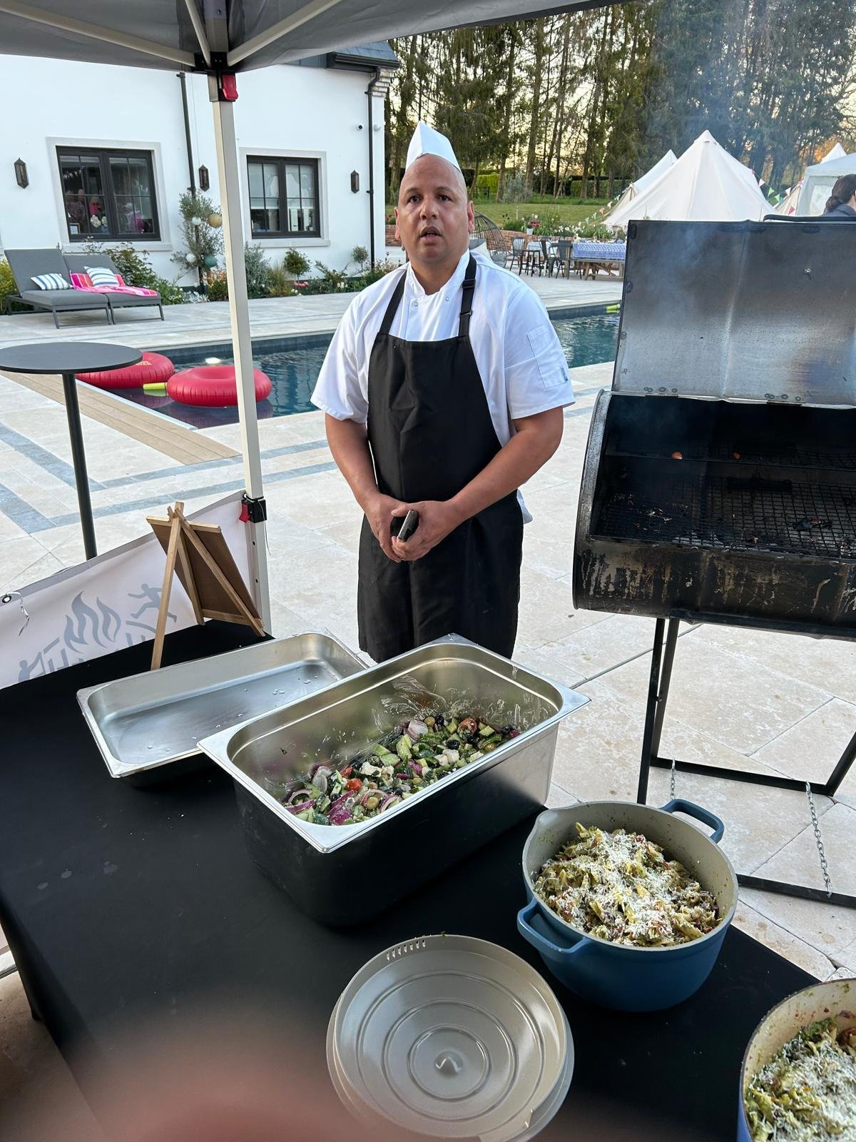 Grill Seekers chef beside an outdoor BBQ smoker and prepared side dishes